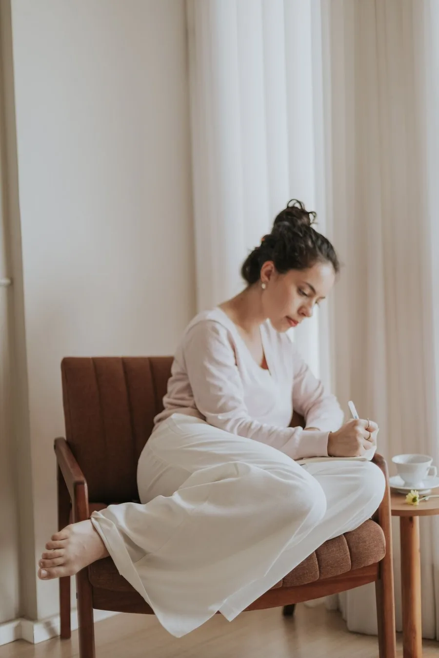 Someone writing in a journal in an armchair by a window