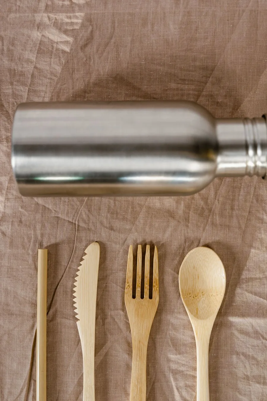 A stainless bottle on linen beside wooden cutlery